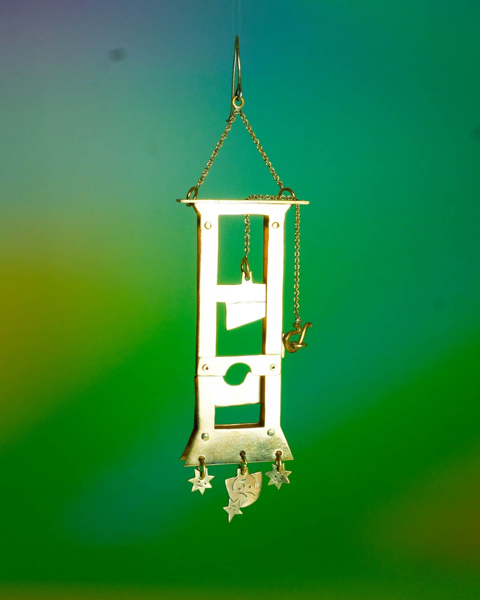Handmade brass guillotine earring with a movable blade, chain mechanism, dangling stars, and a suspended face inspired by the Person Controlled by the Stars series.