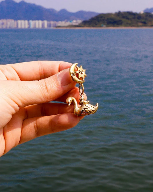 The Swan, cygnet and the moon earring featuring a baby swan riding on its parent, topped with a smiling moon and star. Handmade with lost-wax casting in brass—a tiny ode to love and cosmic connections
