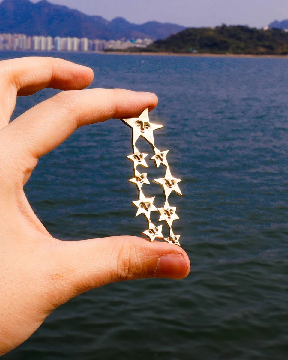 A Puke of Stars handmade earrings — a whimsical cluster of tiny stars, each with a unique face, linking together like cosmic characters. Wax-carved and cast in brass, this one-of-a-kind celestial jewellery piece celebrates connections with playful melancholy