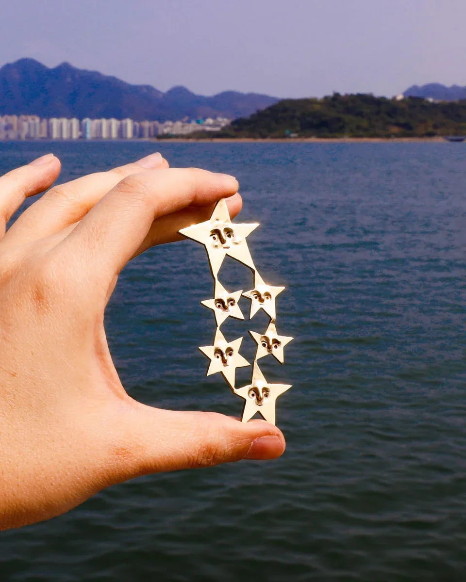 A Mega Puke of Stars’ bold earring — an expansive, intricate network of star characters, each with expressive faces, a statement celestial jewellery . Handcrafted with lost-wax casting in brass, this statement piece merges humour and heartache for those who wear their stories