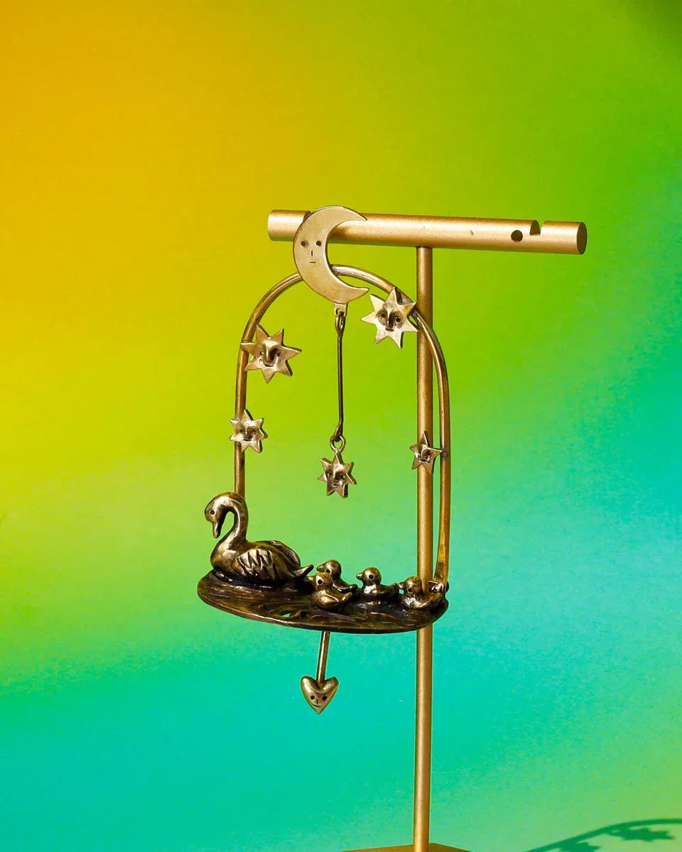 The Swan That Swam the Other Way’ handmade kinetic earrings — a three-part design featuring a moonlit lake, a swan family with four babies (one movable), and a dangling star. Wax-carved and cast in brass, this unique piece embodies memories of solitude and growth.