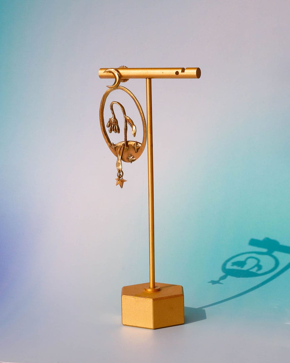 Bloom of a Thousand Stars’ handmade oval earring featuring a dying flower, crescent moon, and falling leaf with dangling star. Lost-wax cast in brass—a wearable poem about grief and cosmic rebirth