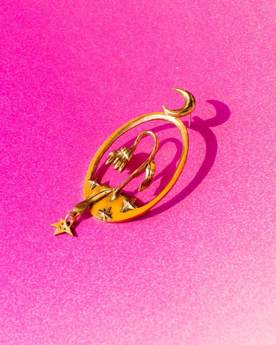 Bloom of a Thousand Stars’ handmade oval earring featuring a dying flower, crescent moon, and falling leaf with dangling star. Lost-wax cast in brass—a wearable poem about grief and cosmic rebirth