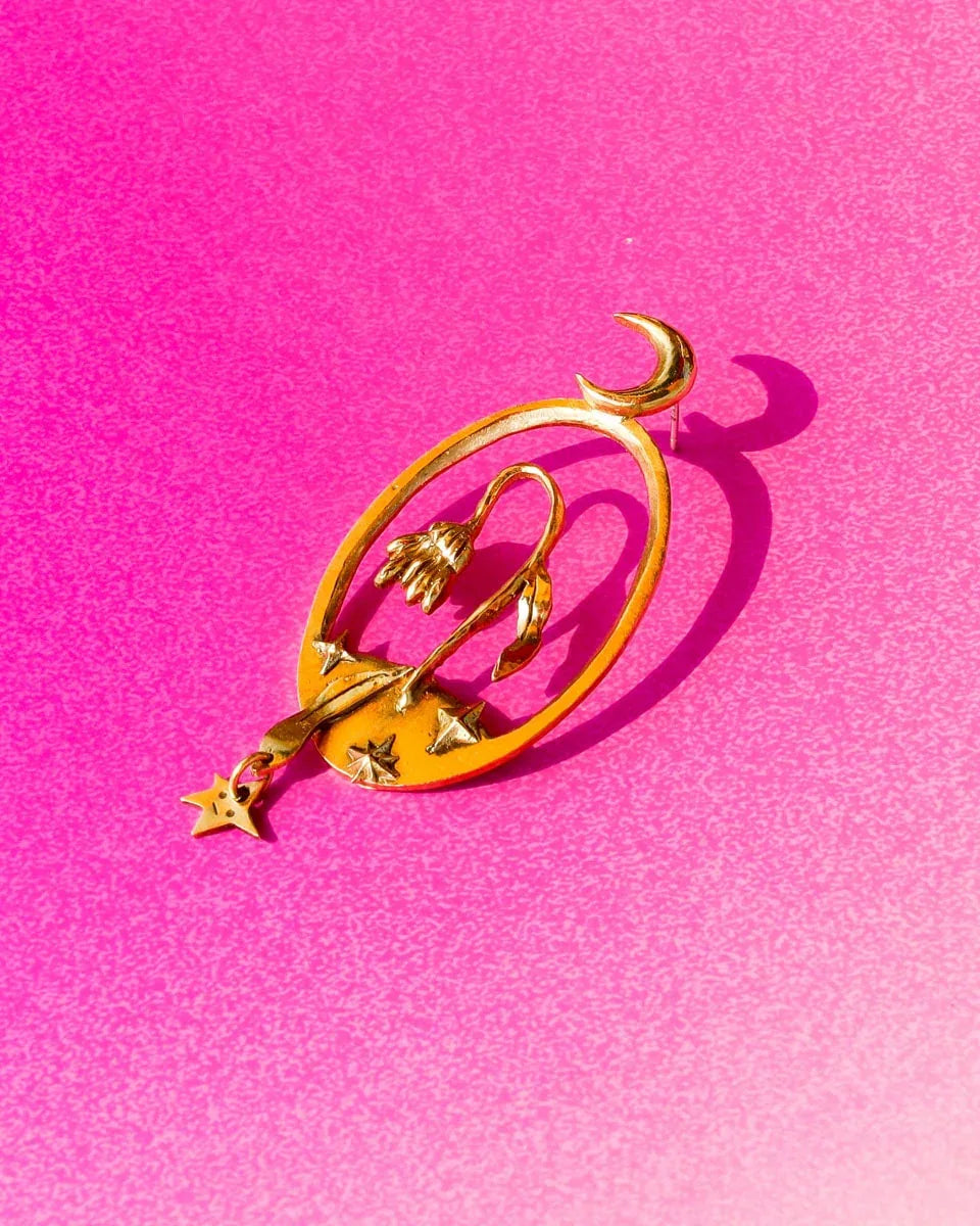 Bloom of a Thousand Stars’ handmade oval earring featuring a dying flower, crescent moon, and falling leaf with dangling star. Lost-wax cast in brass—a wearable poem about grief and cosmic rebirth