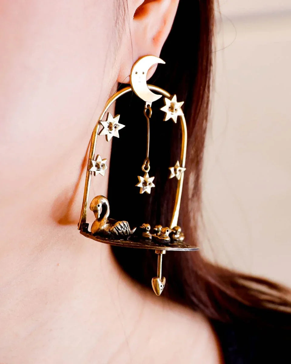 The Swan That Swam the Other Way’ handmade kinetic earrings — a three-part design featuring a moonlit lake, a swan family with four babies (one movable), and a dangling star. Wax-carved and cast in brass, this unique piece embodies memories of solitude and growth.