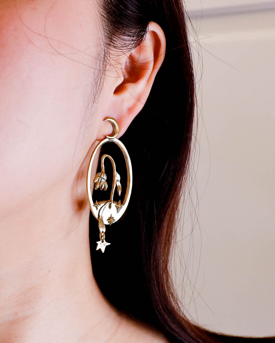 Bloom of a Thousand Stars’ handmade oval earring featuring a dying flower, crescent moon, and falling leaf with dangling star. Lost-wax cast in brass—a wearable poem about grief and cosmic rebirth