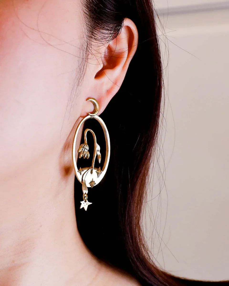 Bloom of a Thousand Stars’ handmade oval earring featuring a dying flower, crescent moon, and falling leaf with dangling star. Lost-wax cast in brass—a wearable poem about grief and cosmic rebirth