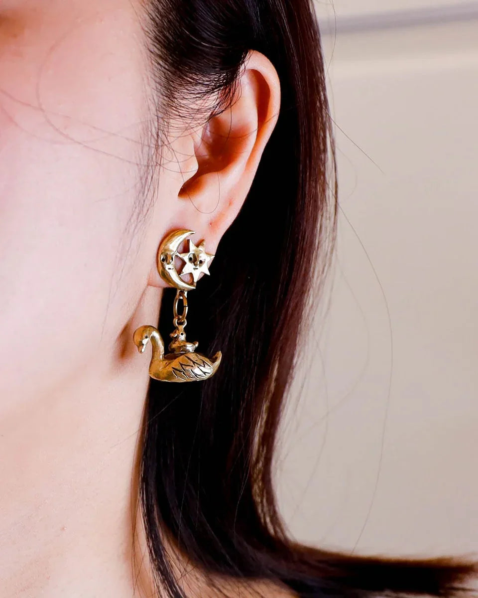 The Swan, cygnet and the moon earring featuring a baby swan riding on its parent, topped with a smiling moon and star. Handmade with lost-wax casting in brass—a tiny ode to love and cosmic connections
