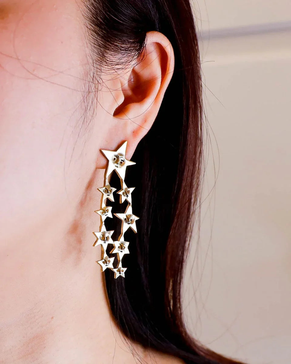 A Puke of Stars handmade earrings — a whimsical cluster of tiny stars, each with a unique face, linking together like cosmic characters. Wax-carved and cast in brass, this one-of-a-kind celestial jewellery piece celebrates connections with playful melancholy