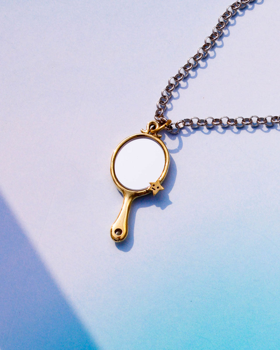 Gold tiny hand mirror pendant on a chain with a tiny star design