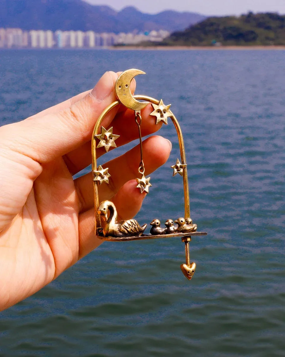 The Swan That Swam the Other Way’ handmade kinetic earrings — a three-part design featuring a moonlit lake, a swan family with four babies (one movable), and a dangling star. Wax-carved and cast in brass, this unique piece embodies memories of solitude and growth.