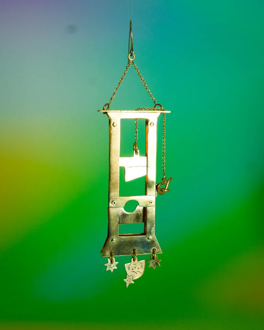 Handmade brass guillotine earring with a movable blade, chain mechanism, dangling stars, and a suspended face inspired by the Person Controlled by the Stars series.