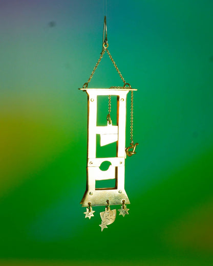 Handmade brass guillotine earring with a movable blade, chain mechanism, dangling stars, and a suspended face inspired by the Person Controlled by the Stars series.