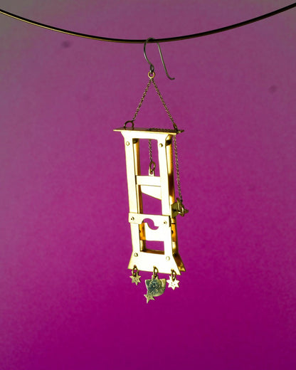 Handmade brass guillotine earring with a movable blade, chain mechanism, dangling stars, and a suspended face inspired by the Person Controlled by the Stars series.