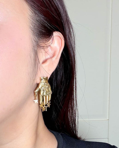 Articulated brass hand earring with dangling stars and sterling silver ear post, worn as sculptural statement jewellery