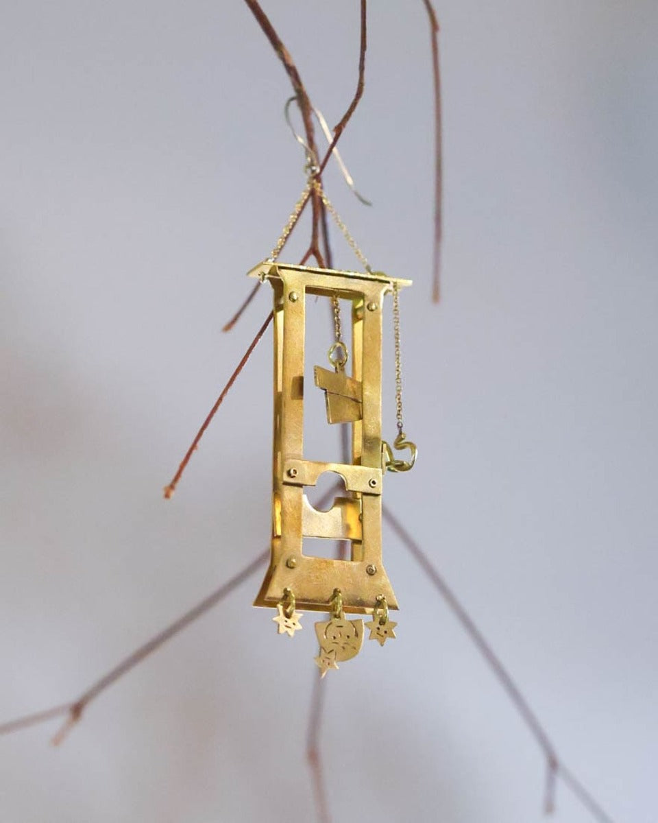 Handmade brass guillotine earring with a movable blade, chain mechanism, dangling stars, and a suspended face inspired by the Person Controlled by the Stars series.