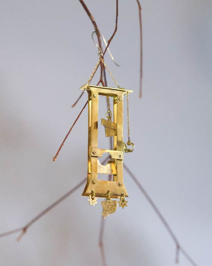 Handmade brass guillotine earring with a movable blade, chain mechanism, dangling stars, and a suspended face inspired by the Person Controlled by the Stars series.