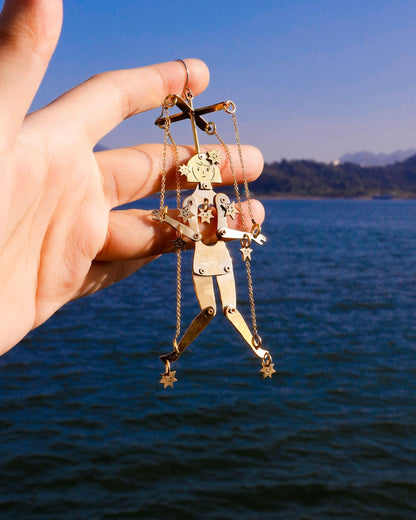 an articulated brass puppet earring "The Person Controlled by the Stars" with moving handsaw joints