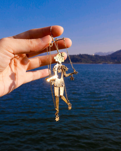 hand holding a gold articulated brass puppet earring "The Person Controlled by the Stars" with moving handsaw joints