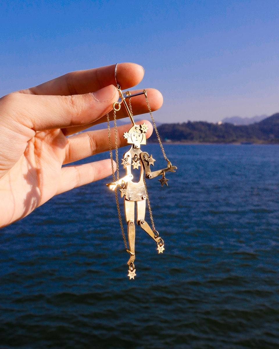 Articulated brass puppet earring "The Person Controlled by the Stars" with moving handsaw joints