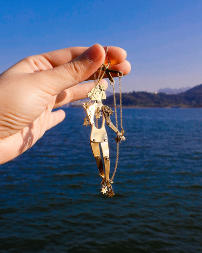 hand holding an articulated brass puppet earring "The Person Controlled by the Stars" with moving handsaw joints