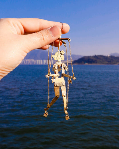 Hand holding a gold an articulated brass puppet earring "The Person Controlled by the Stars" with moving handsaw joints