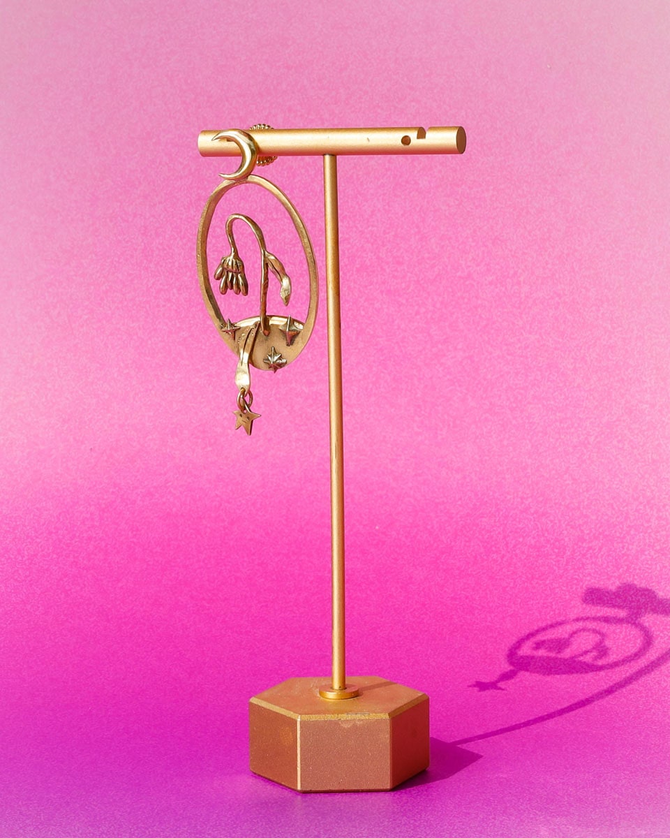 Bloom of a Thousand Stars’ handmade oval earring featuring a dying flower, crescent moon, and falling leaf with dangling star. Lost-wax cast in brass—a wearable poem about grief and cosmic rebirth