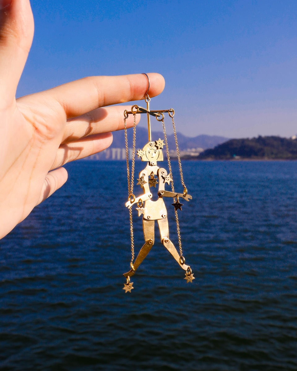 Articulated brass puppet earring "The Person Controlled by the Stars" with moving handsaw joints