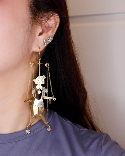 Close-up of a person wearing an articulated brass puppet earring "The Person Controlled by the Stars" with moving handsaw joints