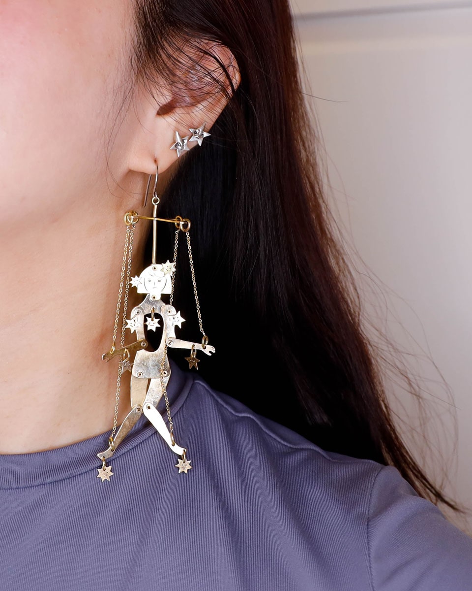 Close-up of a person wearing an articulated brass puppet earring "The Person Controlled by the Stars" with moving handsaw joints