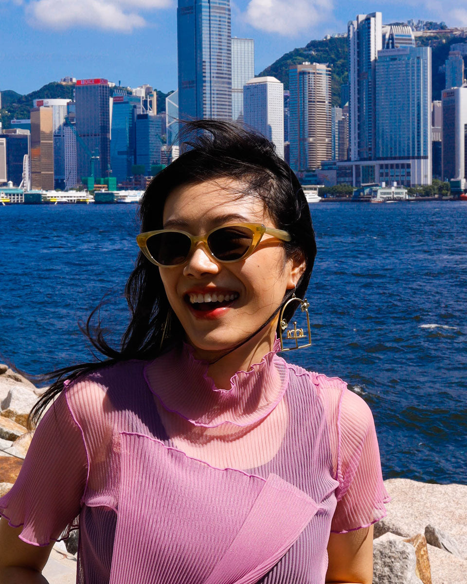 woman wearing brass-framed merry-go-round earring with floral design on the frame, empty playground earring with kinetic element. made by fake plastic love