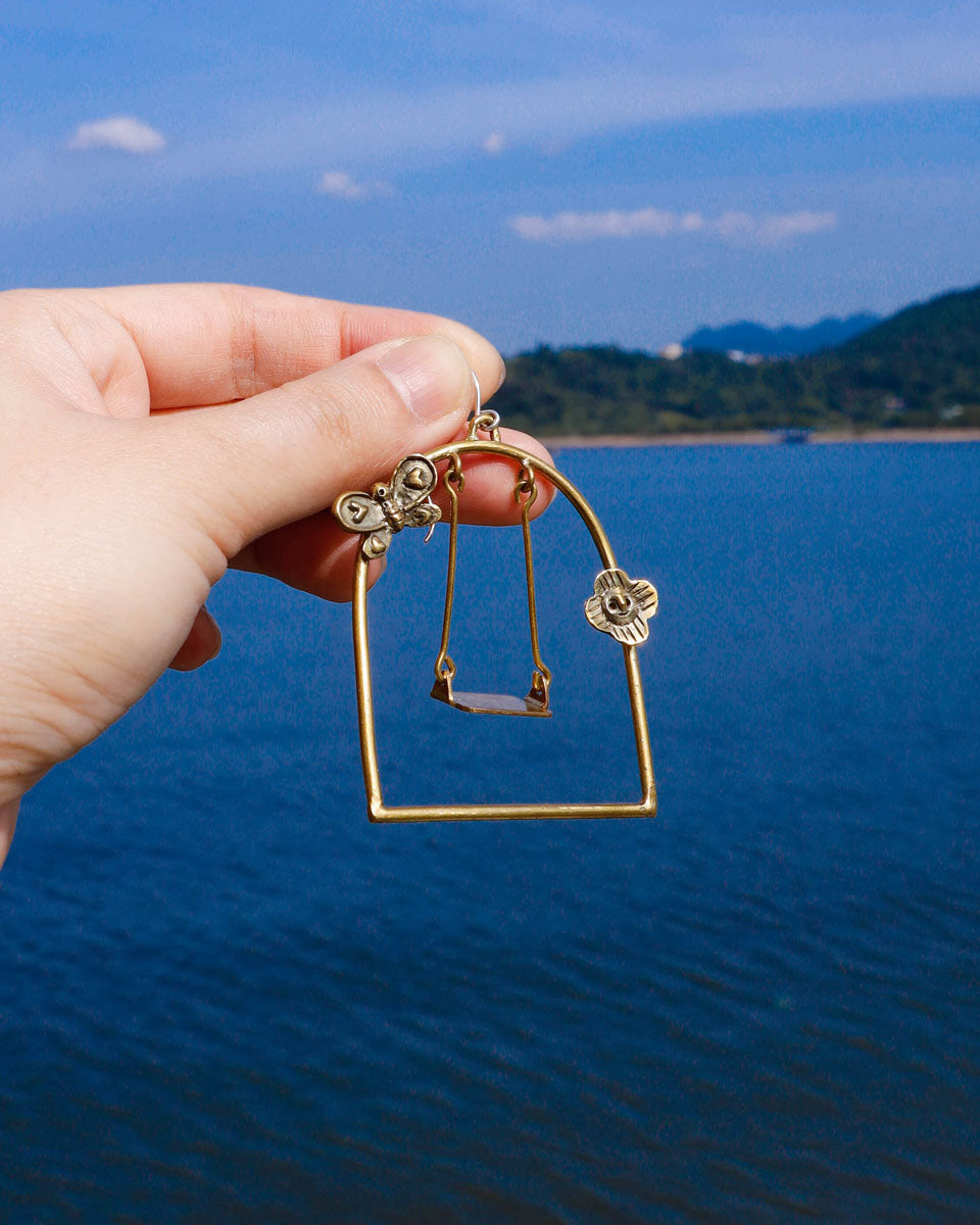 empty playground earring with a moving swing inside a frame with butterfly and flower design, handmade miniature brass jewellery 