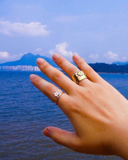 Hand wearing two rings one simple star ring in sterling silver and many stars ring a wide band ring with star designs