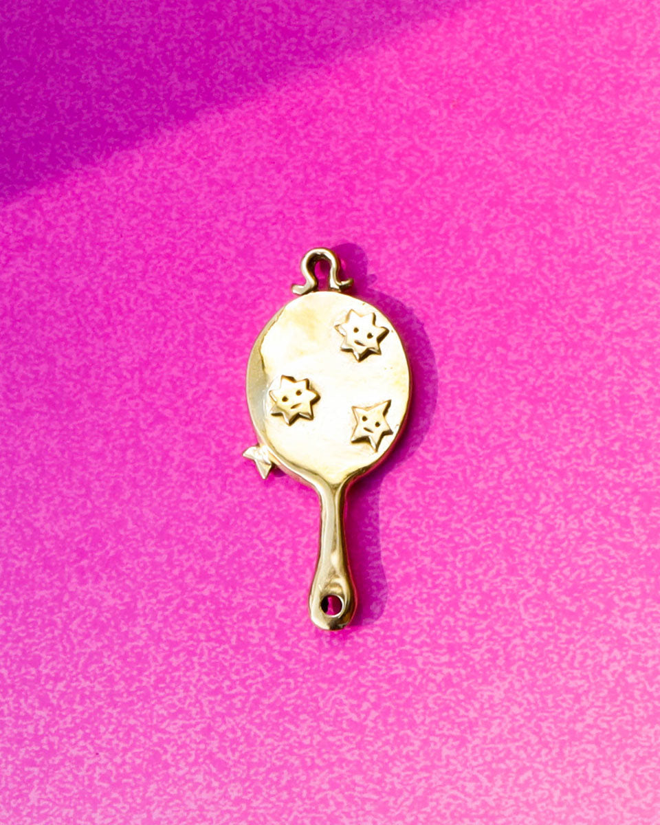 Gold hand mirror charm with star designs on a pink background
