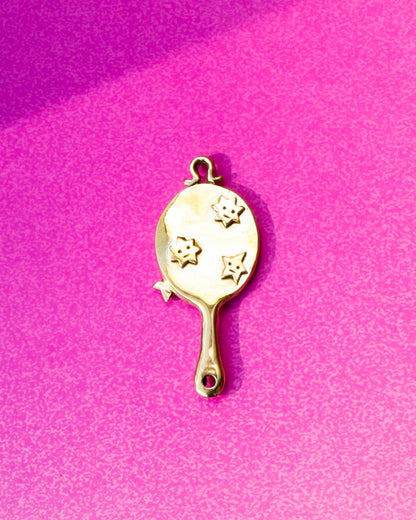 Gold hand mirror charm with star designs on a pink background