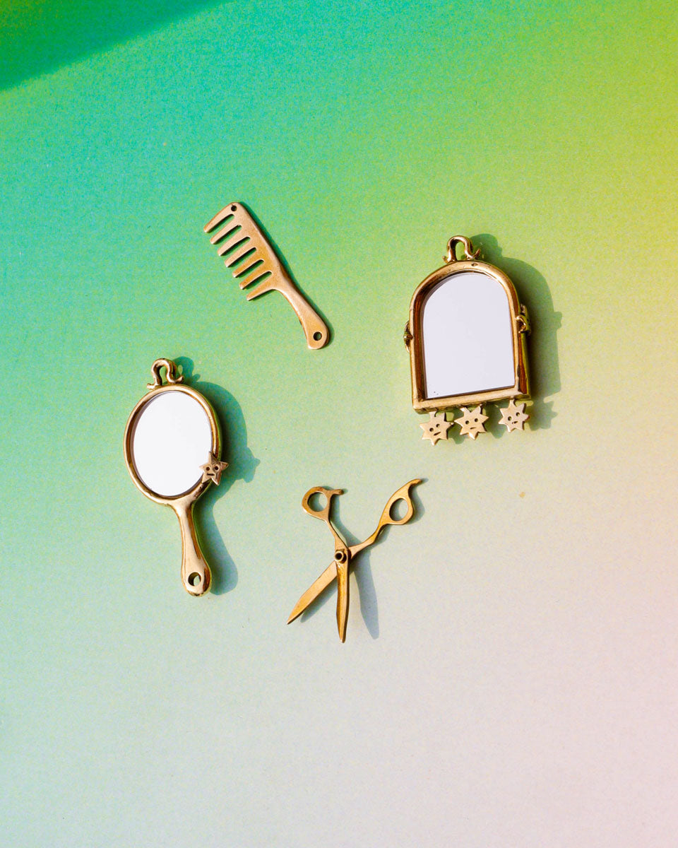 Set of gold hair styling tools including a comb, mirror, and scissors on a gradient background
