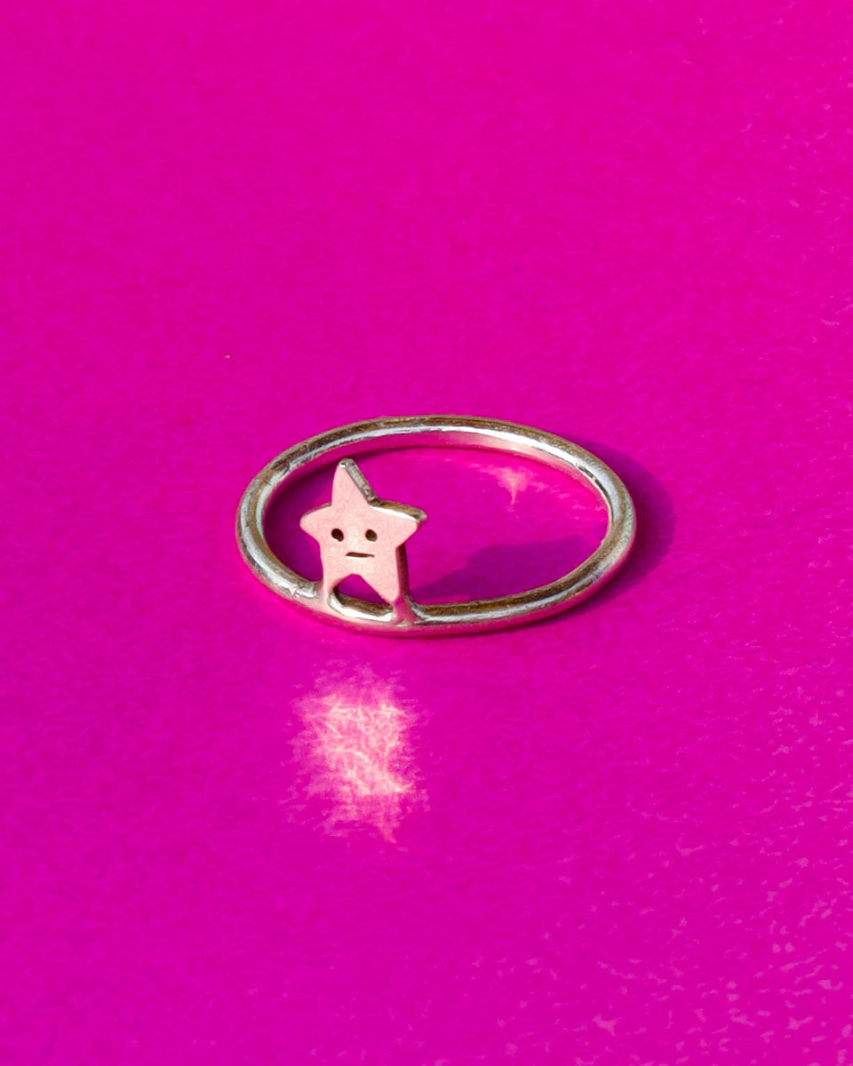 Silver ring with a star-shaped charm on a pink background