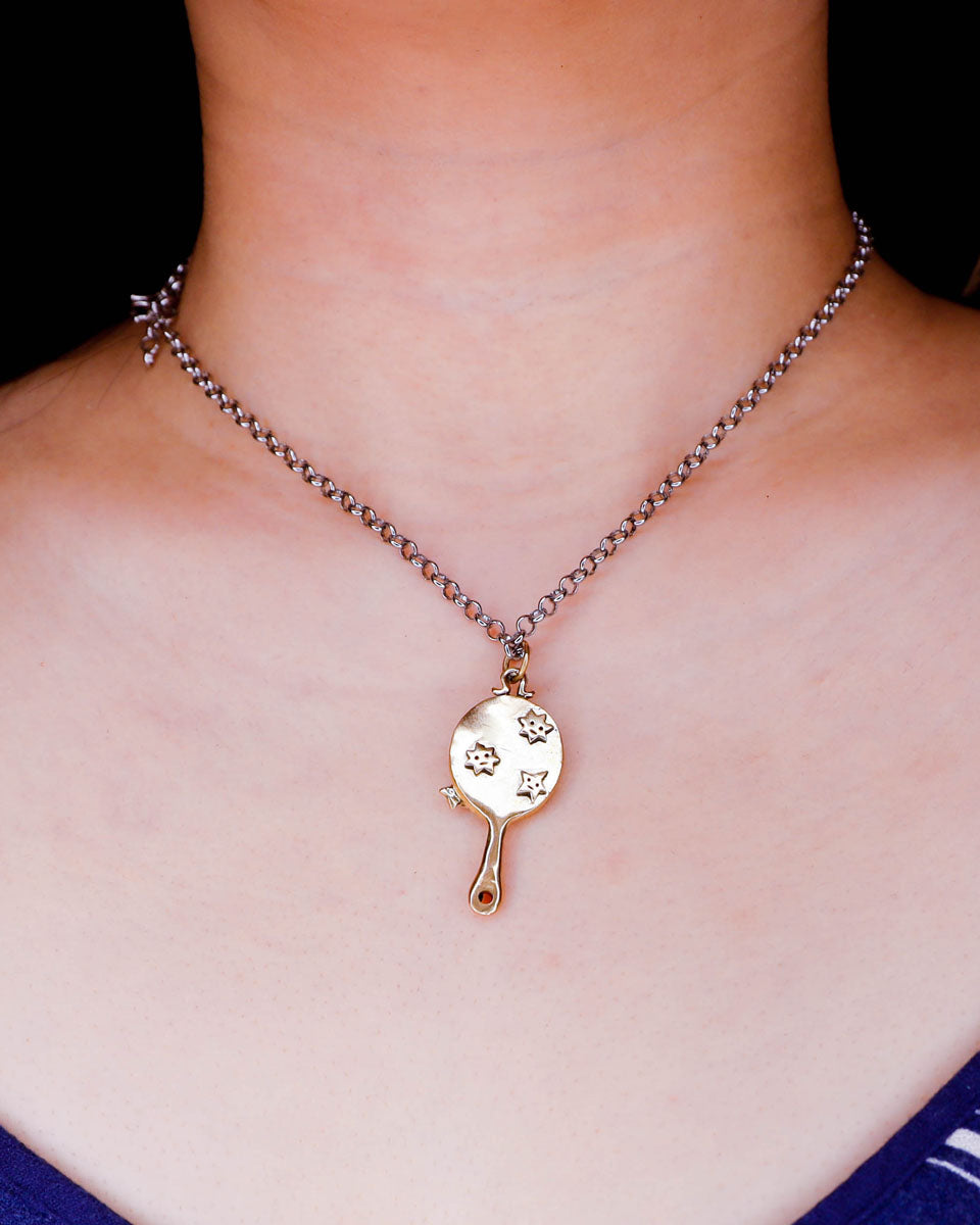 Necklace with a tiny hand mirror pendant with stars designs in brass worn by a person