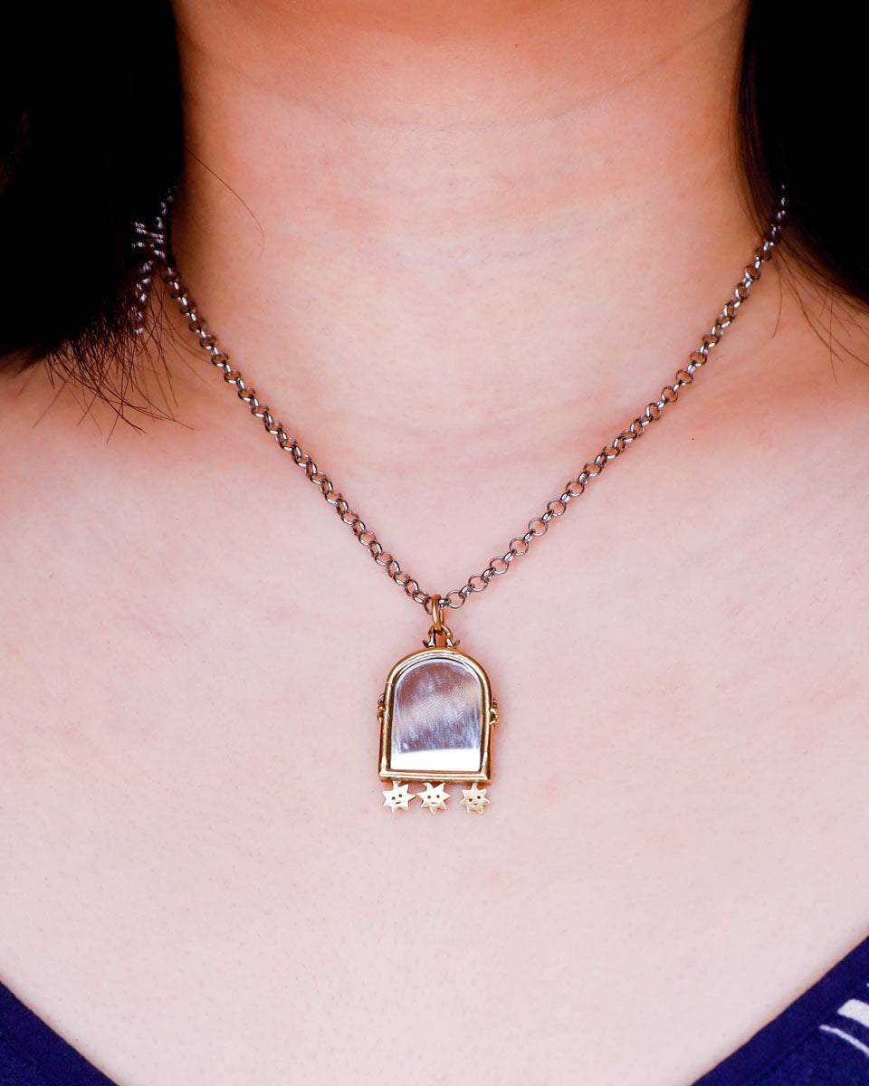 necklace with an arched-shaped mirror with stars design pendant on a person's neck