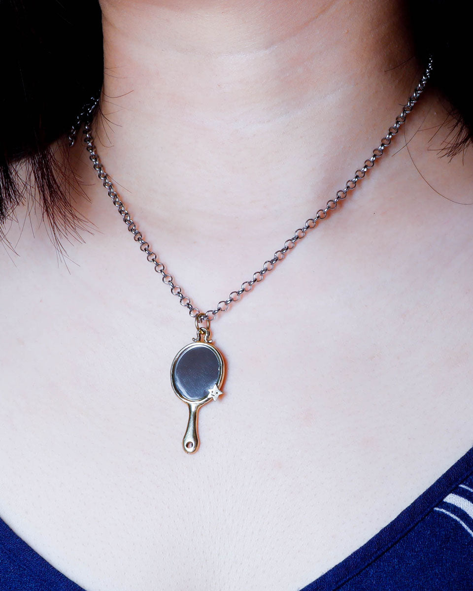 Necklace with a tiny hand mirror pendant in brass worn by a person