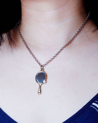 Necklace with a tiny hand mirror pendant in brass worn by a person