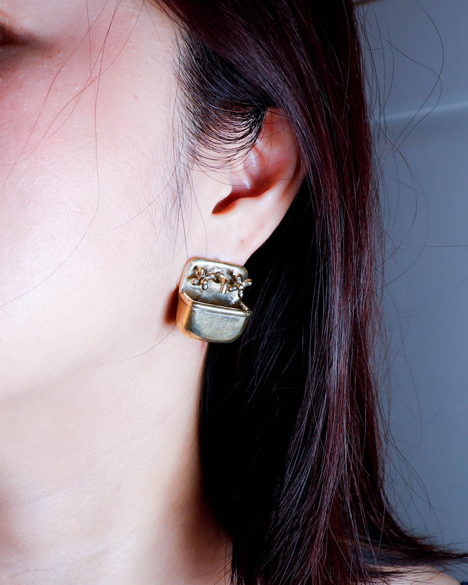 a person wearing a Miniature tiny sink earring in solid brass with sterling silver post, featuring movable faucet knobs and a detailed cast design inspired by a household bathroom sink