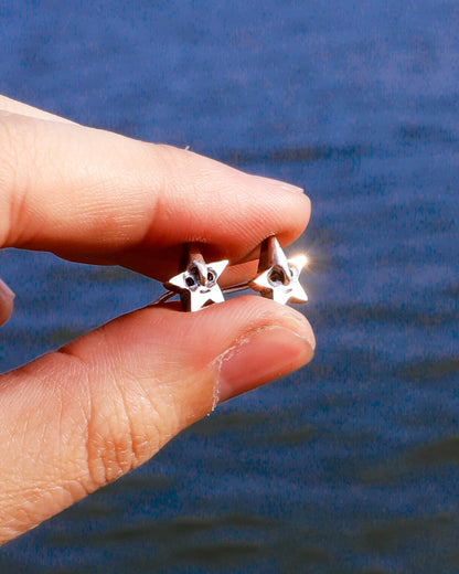 Star-shaped sterling silver earrings held between fingers 