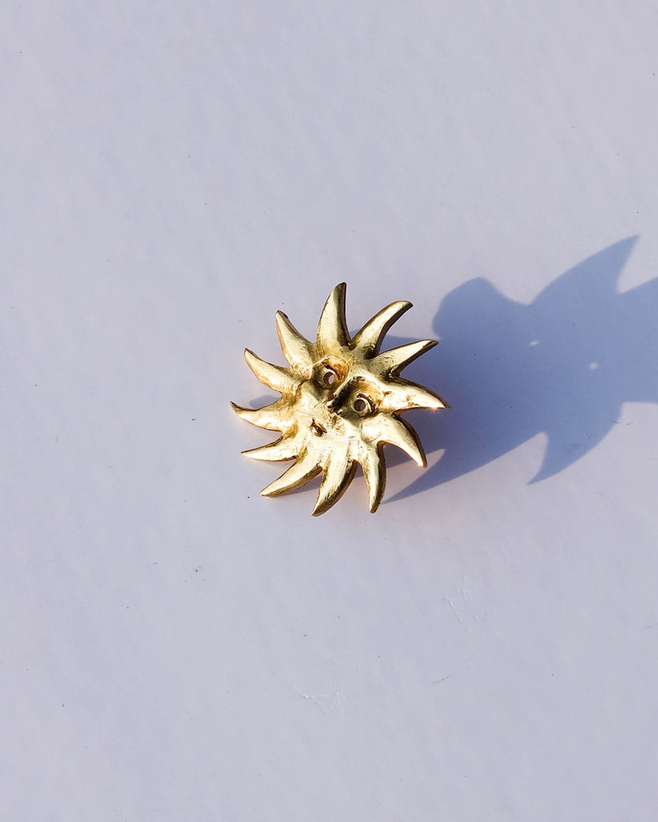 Gold sun-shaped earring on a light gray background