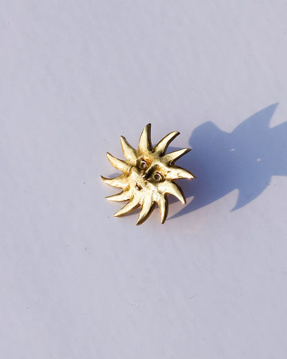 Gold sun-shaped earring on a light gray background