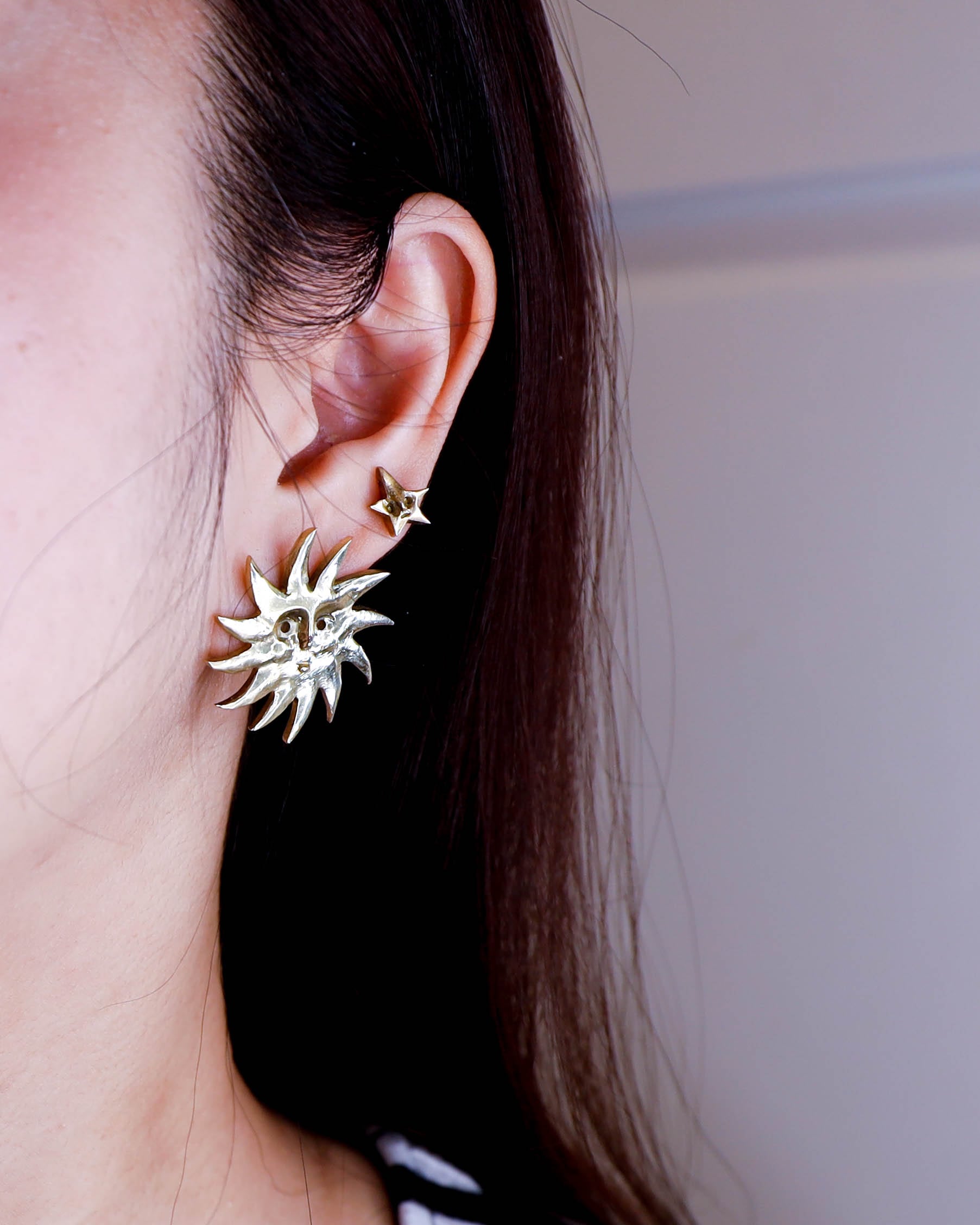 Close-up of an ear wearing a sun and a star-shaped earrings with a plain background