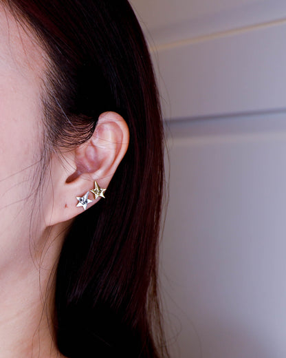 Close-up of an ear wearing two star-shaped earrings in sterling silver and brass